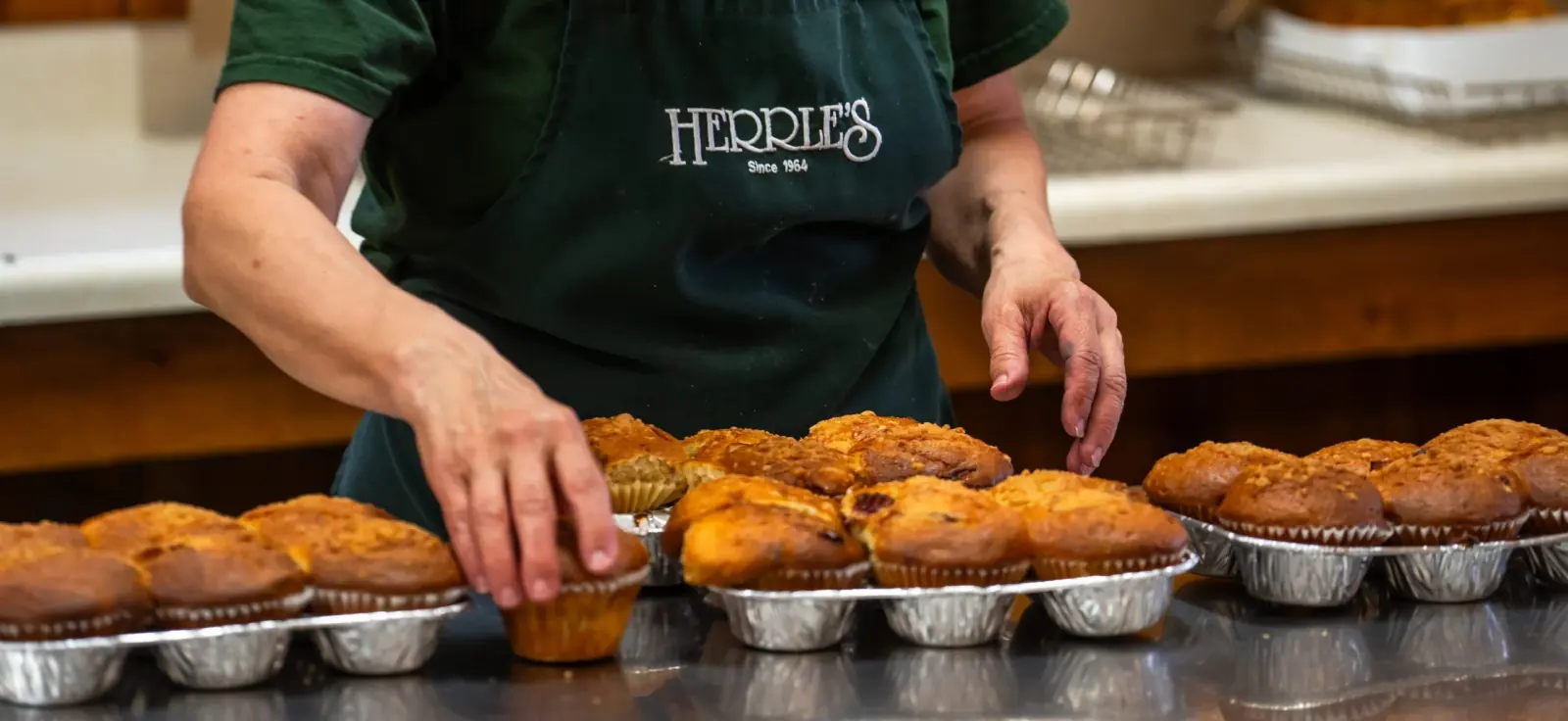 Hands arranging trays of fresh muffins in the bakery