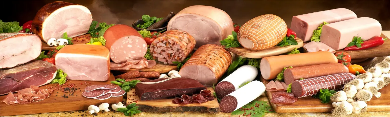 A long spread of deli meats: hams, salamis, sausages and a roast, with mushrooms and herbs