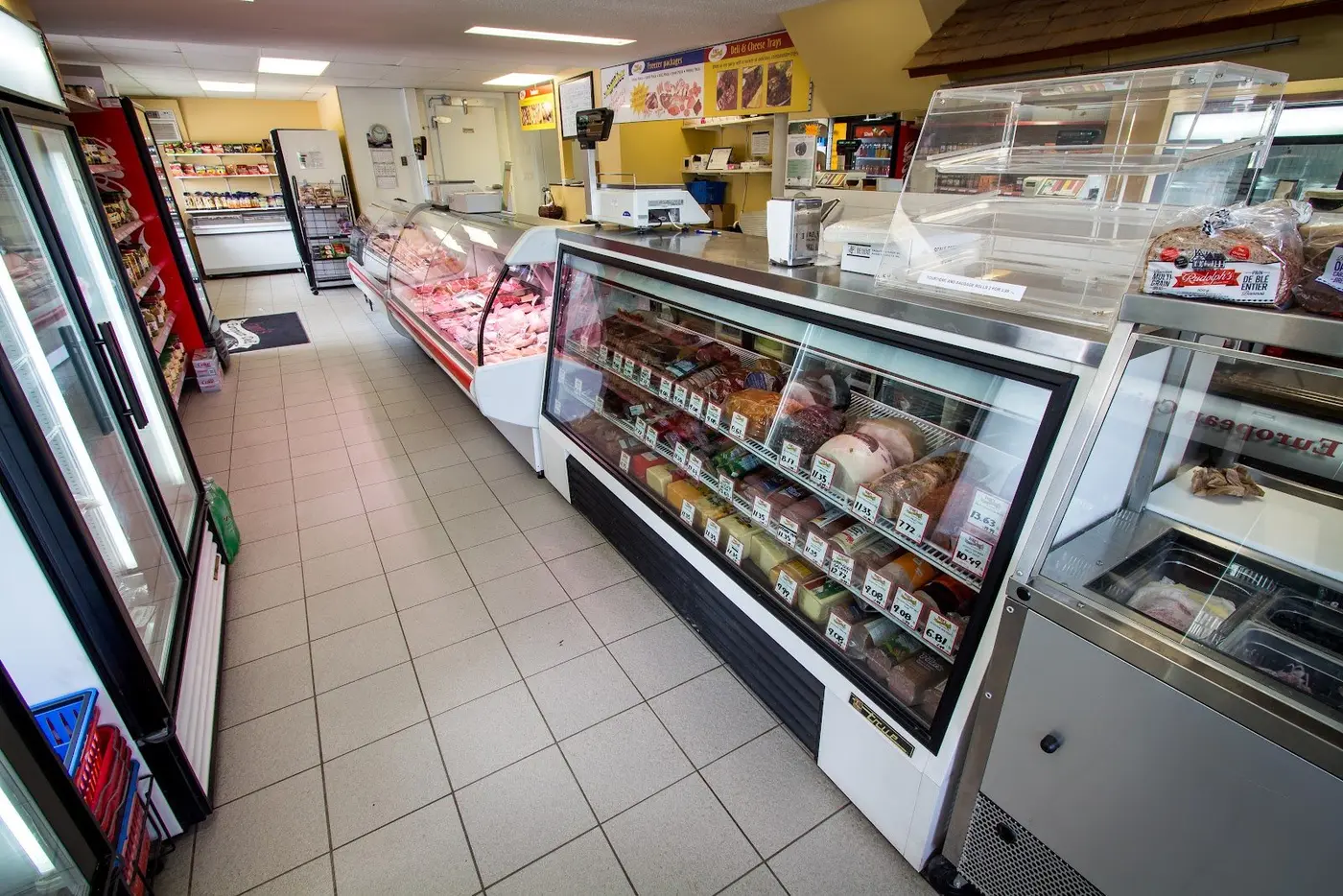 Inside the shop: deli and meat cases along a tiled aisle, with drinks fridges on the left