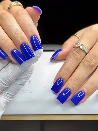Deux mains aux ongles carrés d’un bleu vif et brillant.