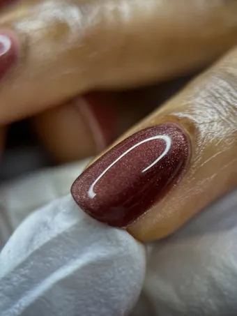 Gros plan d’un ongle bordeaux scintillant réalisé par Lounge beauté by Richie.