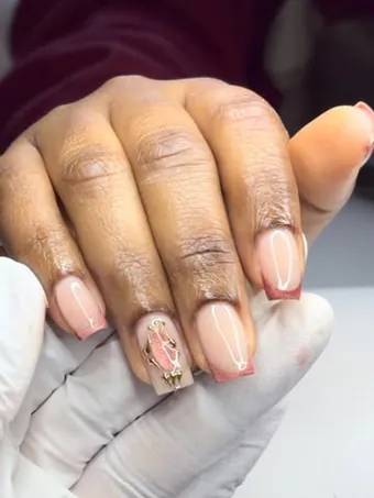Ongles carrés nude aux pointes rose cuivré, un ongle orné d’un bijou doré.
