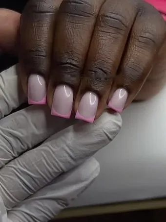 Ongles carrés rose pâle aux pointes rose vif, tenus dans une main gantée.