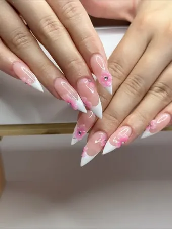 Ongles longs et pointus, nude aux pointes blanches, décorés de petites fleurs roses.