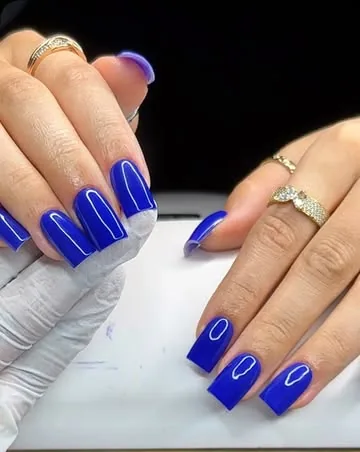 Deux mains aux ongles carrés d’un bleu vif et brillant.