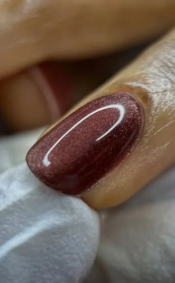 Gros plan d’un ongle bordeaux scintillant réalisé par Lounge beauté by Richie.