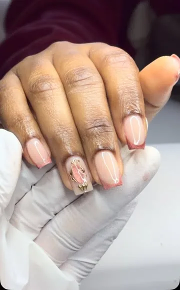 Ongles carrés nude aux pointes rose cuivré, un ongle orné d’un bijou doré.