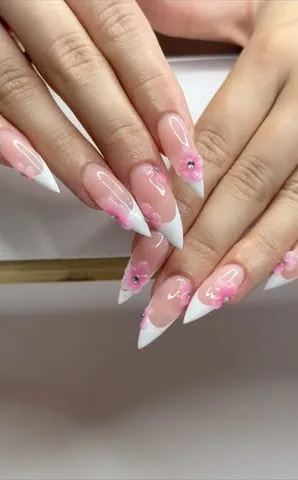 Ongles longs et pointus, nude aux pointes blanches, décorés de petites fleurs roses.