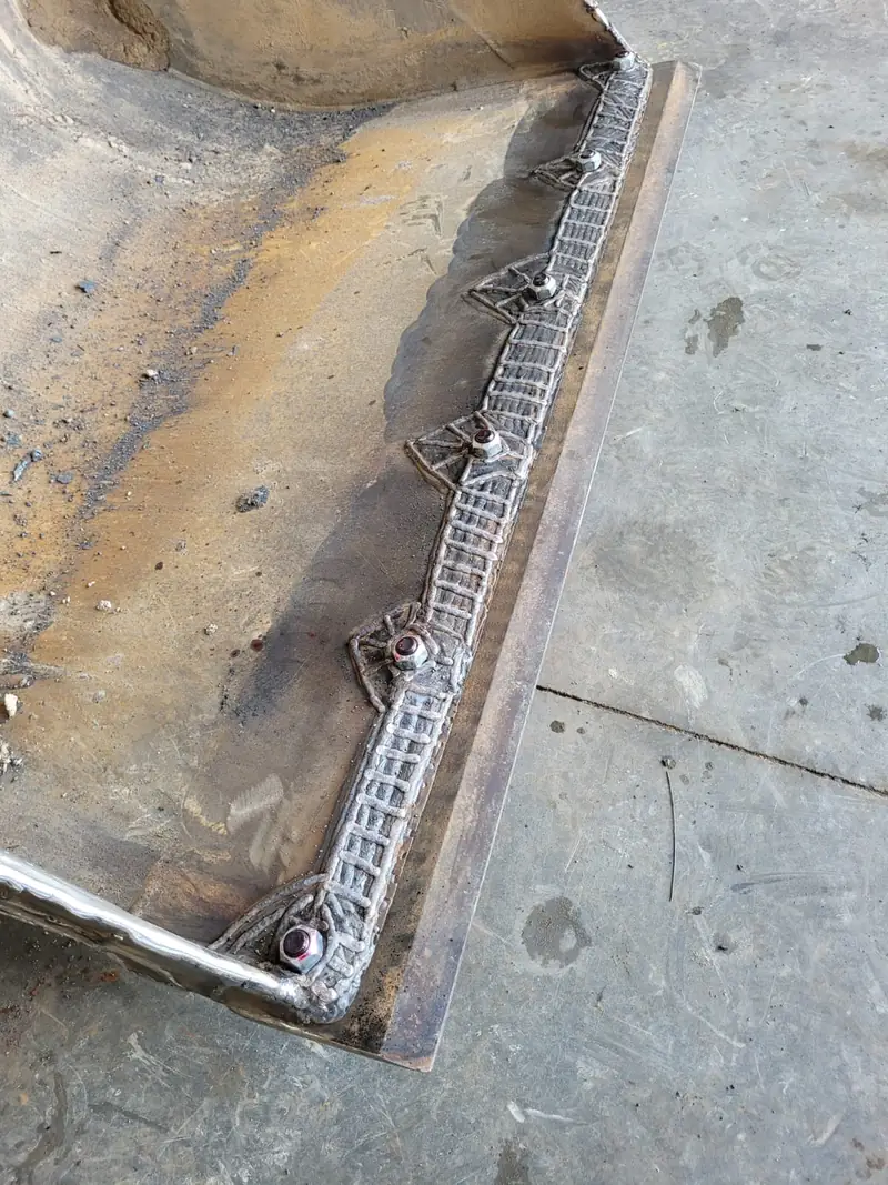 Bucket edge with a new cutting edge bolted on and hard-surfacing weld beads laid in a ladder pattern