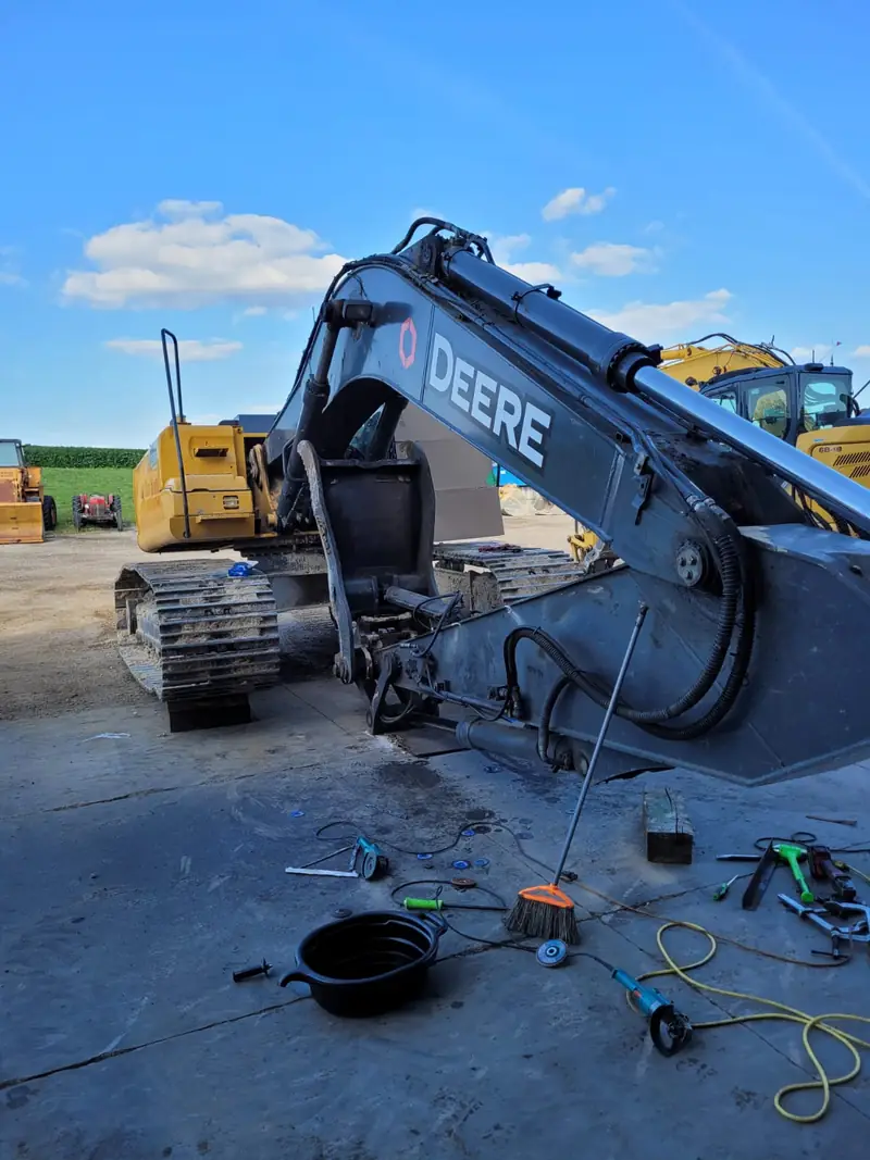 Excavator in the PineGrove yard after its boom repair, with welding cables and tools on the ground