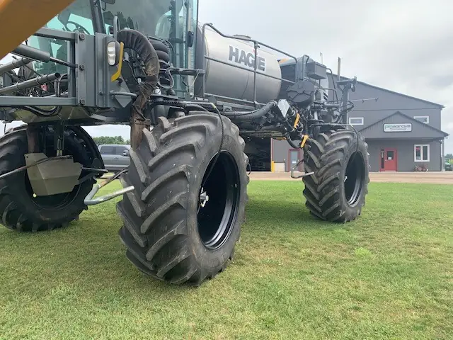 Sprayer with air lines running to the wheel hubs, parked on grass by the shop