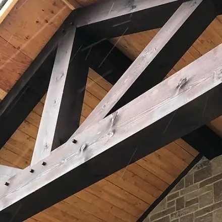 Close view of dark stained truss beams crossing under a tongue-and-groove wood porch ceiling