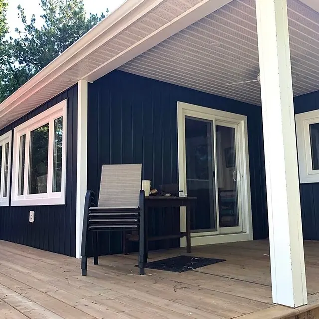 A covered cottage deck with navy vertical siding, white soffit overhead, white trim and a sliding door