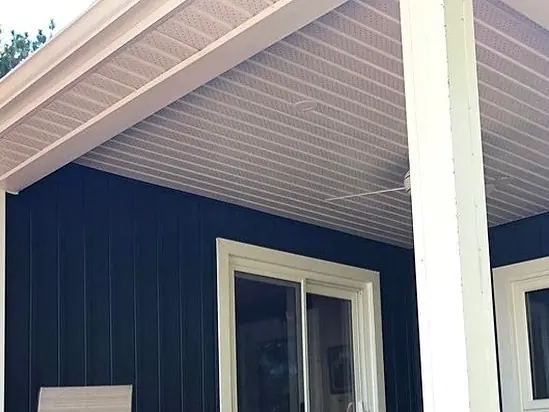 White vented soffit and fascia over a covered cottage deck with navy vertical siding, a white post and a sliding door